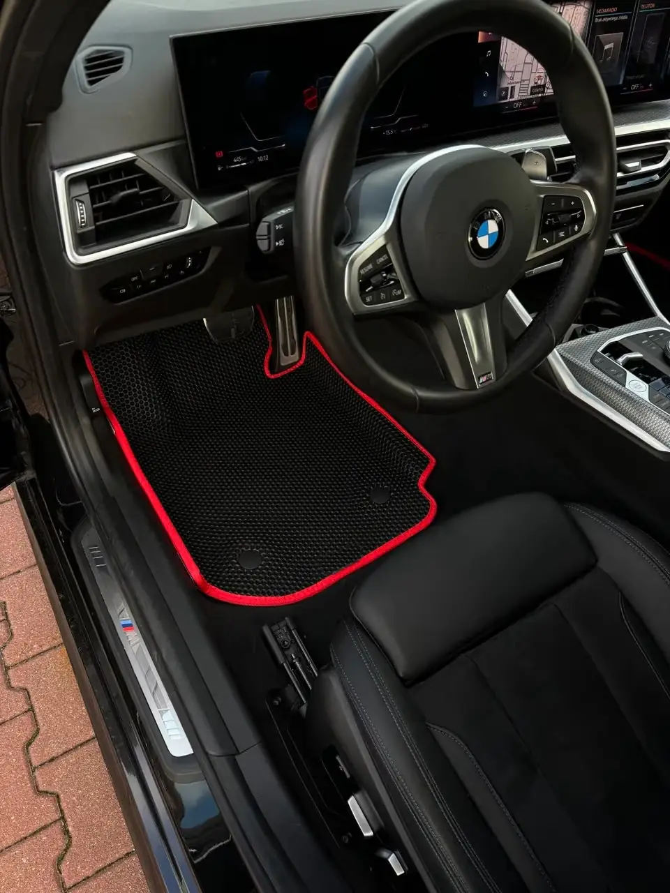 Czarny dywanik EVA z czerwonym obszyciem w BMW, struktura plastra miodu, strona kierowcy.